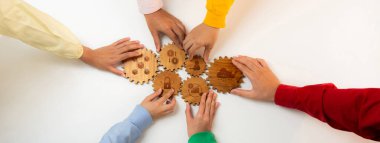 A dynamic scene showcasing hands working together to assemble wooden gears on a clean white background, representing collaboration, unity, and problem solving within a team. Amity