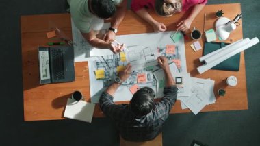 İnşaat mühendislerinin masa başında proje planıyla otururken tablet kullanarak ev yapısını dizayn etmelerine tepeden aşağı bir bakış açısı. Ekip planlama ve inşaat hakkındaki fikirlerin havadan görüşü. Sempozyum.