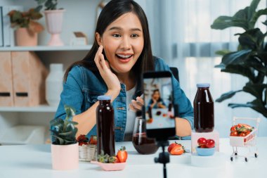 Gülümseyen, güzel Asyalı genç, lezzetli karışık çilek ve kiraz suyu detoksu içeceklerini inceleyen, sosyal medyada özel promosyon satışı için sağlıklı ürünler sergileyen. Taktik.