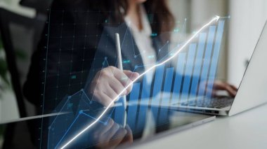 A focused business professional analyzes financial data on a laptop while referencing a digital growth chart, showcasing a modern workspace and commitment to success. Copula
