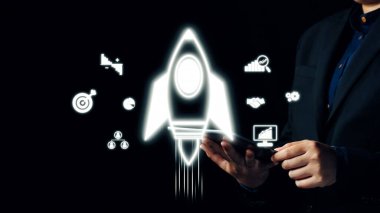 Bir iş adamı elinde bir tablet tutarken fütüristik roket imgeleri, güçlü ve zarif bir tasarımla büyümeyi, yeniliği ve dijital stratejiyi sembolize eder. Dörtgen