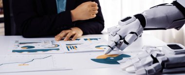 Bir insan ve robot elin veri analizinde işbirliği yaptığı modern bir ofis sahnesi. İş görüşlerini vurgulayan grafikler ve grafiklerle raporlara odaklan. Noogenesis
