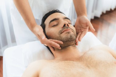 Beyaz adam stres önleyici kafa masajından ve lüks bir tatil beldesi veya otel spa salonundaki modern ışık ortamında yüz güzelliği eğlencelerini şımartmaktan hoşlanıyor. Sessiz.