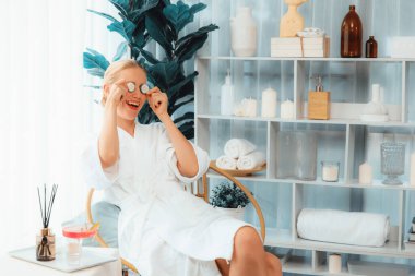 Elinde taze salatalık dilimleri tutan ve bornoz giyen bir kadın tatil köyünde ya da otelde lüks yüz derisi kaplıcalarının tadını çıkarıyor. Yüz ve güzellik tedavisi için cilt bakımı. Sessiz.