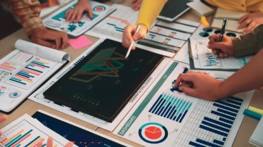 A diverse business team engages in collaborative financial analysis using a digital tablet to review graphs and charts. The modern office setting enhances productivity and creativity. SACTR