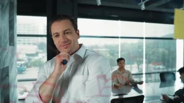 Akıllı lider işadamı cam tahtanın önünde proje başlatmayı düşünüyor. Gülümseyen erkek proje yöneticisi yaratıcılık pazarlama stratejisini gösteren renkli yapışkan notlara bakıyor. Yönlendirici.