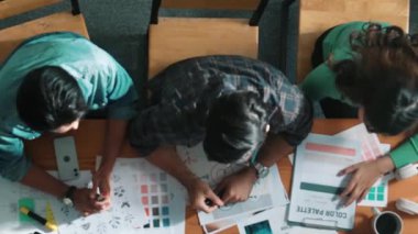 Tasarımcı fikirleri yazarken proje yöneticisinin yukarıdan aşağıya bakan görüntüsü. Akıllı iş adamları logo tasarımı fikrini açıklarken tasarımcılar palete bakarken temayı seçiyorlar. Sempozyum.