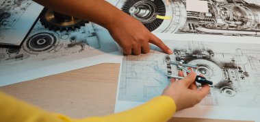 Bu resim mekanik çizimler yapmakla meşgul elleri gösteriyor, profesyonel bir çalışma alanında teknik araçlar ve vitesler, hassasiyet ve yaratıcılığı vurguluyor. SACTR