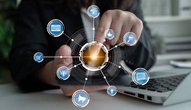 A business professional engages with a digital interface filled with various technology icons on a laptop in a modern office environment, representing innovation and connectivity. Crux