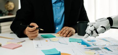 Robot bir kolla iş görüşmesi yapan bir profesyoneli gösteren eşsiz bir ofis sahnesi. Konferansta çizelgelerin analiz edilmesi ve teknolojik işbirliğinin geliştirilmesi üzerinde duruluyor.