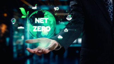 Bir işadamı, sürdürülebilirliği ve yeniliği temsil eden ve modern bir ofis alanında geçen ikonlarla çevrili net bir sıfır mesajı içeren holografik bir küre sunar. Dörtgen