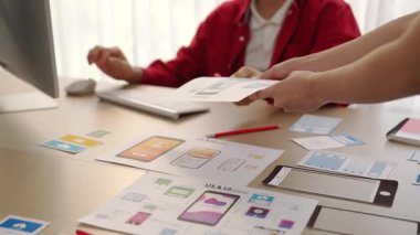 Mobil uygulama için kullanıcı arayüzü prototipini ofis çalışma alanındaki akıllı yöneticiye sunan mükemmel bir şirket çalışanı. UX UI tasarımcısı kağıt üzerinde simge tasarımının işlevini açıklıyor. Sinerjik