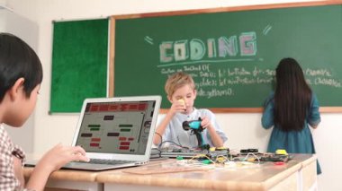 Kafkas arkadaşı STEM sınıfında elektrik panosunu tamir ederken Asyalı çocuk kodlama programı. Enerjik öğrenci kodlama mühendisliği komut yazarken ve yapay zeka yazılımını programlarken tahtada duruyor. Pedagoji.