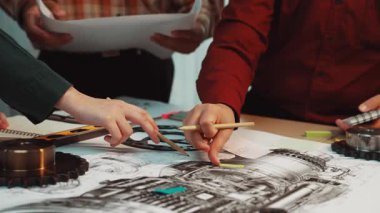 A diverse group of professionals collaborates on an engineering project, discussing detailed technical drawings and utilizing tools, fostering innovation and ideas in a modern workspace. SACTR