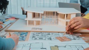 A collaborative architectural workspace showcasing hands engaged in model development, surrounded by blueprints and sketches for innovative design projects. SACTR