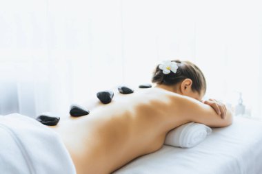 Lüks tatil köyündeki kaplıcalarda sıcak taş masajı. Gün ışığı sükunet ortamında, mutlu kadın müşteri bazalt taş masajından zevk alıyor. Rahatlatıcı bir sıcaklıkla vücudun üzerinde süzülüyor. Sessiz.