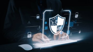 Dijital güvenliğin, karanlık bir ortamda siber tehditlere karşı korunmayı temsil eden parlayan bir kalkan sembolü olan bir klavyeye yazı yazan odaklı tasviri. Dörtgen