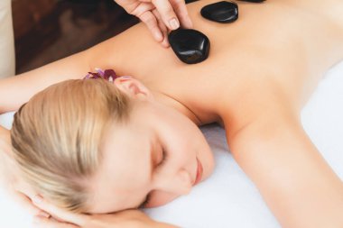 Lüks tatil köyündeki kaplıcalarda sıcak taş masajı. Gün ışığı sükunet ortamında, mutlu kadın müşteri bazalt taş masajından zevk alıyor. Rahatlatıcı bir sıcaklıkla vücudun üzerinde süzülüyor. Sessiz.