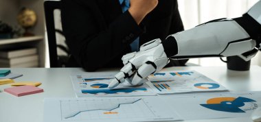 Bir robot kolu, otomasyon ve teknolojinin modern çalışma alanına entegrasyonunu gösteren bir iş toplantısı sırasında grafikler ve grafiklerle uğraşır. Noogenesis