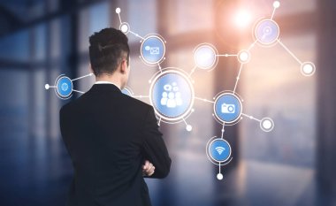A businessman stands with arms crossed, observing digital networking icons in a modern office setting. The image captures themes of connectivity, technology, and innovation. Tessel