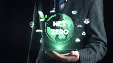 Bir işadamı, sürdürülebilirlik ve çevresel sorumluluğun önemini sembolize eden yeşil bir küre ve net sıfır konseptin dijital görüntüsünü akıllı telefona sunuyor. Dörtgen