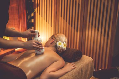 Sıcak bitkisel top spa masaj vücut tedavisi, masör kadın vücuduna nazikçe şifalı bitki torbası bastırıyor. Aromaterapi tesisinin sakinliği ve dinginliği kaplıca salonundaki mumların sıcacık ışığında. Sessiz.