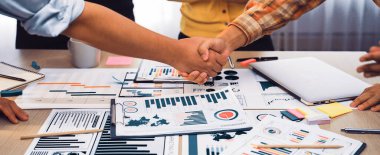 Çeşitli iş belgelerinin, çizelgelerin ve raporların el sıkışmasını gösteren dinamik bir sahne profesyonel bir ortamda işbirliği ve ortaklığı sembolize ediyor. SACTR