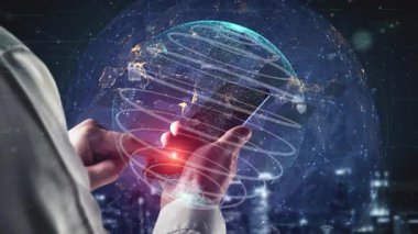 A person holds a smartphone while interacting with a digital globe surrounded by icons. This visual represents modern technology and global connectivity in a futuristic context. Xenic