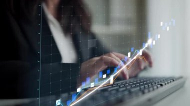 A businesswoman focuses on data trends with a graphical overlay, symbolizing financial growth in a modern office environment while using a computer keyboard. Copula
