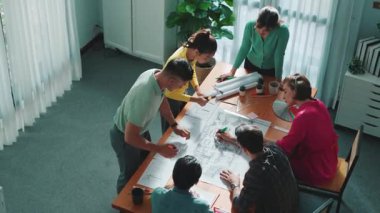 İnşaat mühendisi ekibinin renkli paletlerle toplantı masasında plan yazışının en üst görüntüsü. Yönetici proje planlarına bakarken bir grup zeki insan plan yapıyor ve not alıyor. Sempozyum.