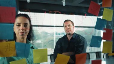 Profesyonel iş adamları yaratıcı pazarlama fikrini modern ofiste tartışırlar. İş adamları cam tahtada yapışkan notlar kullanarak finansal plan üzerinde çalışıyor. Yönlendirici.