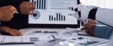 Modern bir iş toplantısı sahnesi, insan eliyle ekip çalışması ve dijital tablette dinamik grafikleri ve grafikleri analiz eden bir robot kol yenilikleri vurguluyor.