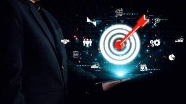 Bir işadamı, çeşitli iş analitik grafikleri, strateji, yönetim ve teknoloji entegrasyonunu sembolize eden bir hedef ikonu gösteren dijital bir tablet tutuyor. Dörtgen
