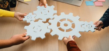 Modern ofis ortamında işbirliği yapan, takım çalışmasını, yenilikleri ve yaratıcı bir çalışma ortamında problem çözmeyi sembolize etmek için kağıt vites tutan bir grup birey. SACTR