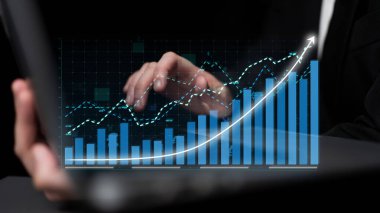 A businessman uses a laptop to analyze financial data with digital graphs. The image represents modern workspace technology, growth, and strategic planning. Impute