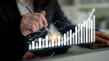 A business professional uses a tablet to analyze financial data trends displayed through interactive graphs and charts in a modern office setting. Impute