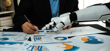 Bir insan ve robotik el, bir iş toplantısı sırasında veri analizine girişerek, grafikler ve grafikler yoluyla modern işyerlerinde teknolojinin entegrasyonunu gösteriyor.
