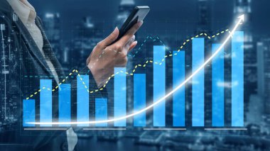 A professional businessman holding a smartphone stands against a city skyline, with financial graphs highlighting growth and success in the business sector. Copula