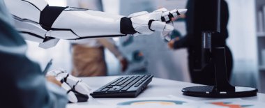 Robotik bir kol modern bir ofiste bir bilgisayara doğru uzanıyor, bir iş görüşmesi sırasında teknoloji ve insan işbirliğini gösteriyor. Noogenesis