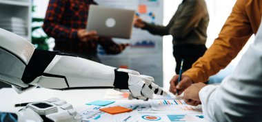 Robot bir kol, insan meslektaşlarına modern bir ofiste yardım etmek için uzanıyor, yaratıcı projeler ve stratejik tartışmalarda teknoloji ve takım çalışması arasındaki sinerjiyi somutlaştırıyor. Noogenesis