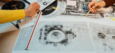 Bu resim, ellerin teknik çizimler ve mekanik bileşenler ile meşgul olduğu, takım çalışmasını ve tasarım süreçlerindeki yenilikleri gösteren bir ortak mühendislik oturumu yakalar. SACTR