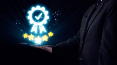 Takım elbiseli bir iş adamı, modern teknoloji ortamında başarı, kalite ve yeniliği temsil eden yıldızlı bir dijital ödül sembolü sergiliyor. Dörtgen