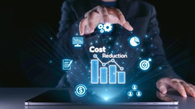 Bir işadamı, modern bir çalışma alanındaki finans ve teknolojik yenilikleri vurgulayarak, bar grafikleri ve simgeler kullanarak dijital bir maliyet azaltma kavramını resmetmektedir. Dörtgen