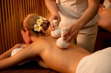 Sıcak bitkisel top spa masaj vücut tedavisi, masör kadın vücuduna nazikçe şifalı bitki torbası bastırıyor. Aromaterapi tesisinin sakinliği ve dinginliği kaplıca salonundaki mumların sıcacık ışığında. Sessiz.