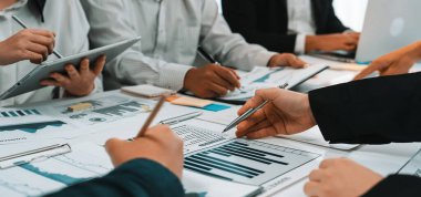 Modern bir ofisteki finansal raporları ve veri görsellemelerini incelemekle uğraşan çeşitli bir iş ekibi. İşbirliği ve analiz stratejik kararlar için içgörü kazandırır. SACTR