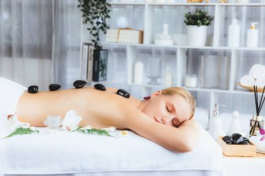 Lüks tatil köyündeki kaplıcalarda sıcak taş masajı. Gün ışığı sükunet ortamında, mutlu kadın müşteri bazalt taş masajından zevk alıyor. Rahatlatıcı bir sıcaklıkla vücudun üzerinde süzülüyor. Sessiz.