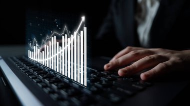 A businessman is focused on a laptop as digital growth charts rise in a dark environment, symbolizing financial insights and data analysis for professional success. Impute