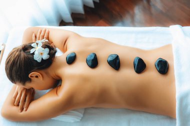 Lüks tatil köyündeki kaplıcalarda sıcak taş masajı. Gün ışığı sükunet ortamında, mutlu kadın müşteri bazalt taş masajından zevk alıyor. Rahatlatıcı bir sıcaklıkla vücudun üzerinde süzülüyor. Sessiz.