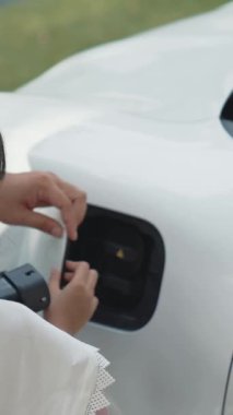İlerici baba-kız elektrikli araç şarj istasyonundan fiş takıyor. Geleceğin çevre dostu arabası yenilenebilir temiz enerji kaynağıyla çalışıyor..