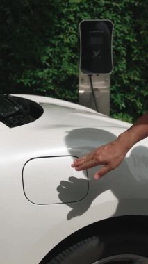 İlerici adam elektrikli aracına elektrik kablosu takıyor. Ev şarj istasyonundan EV arabası. Çevreyi korumak için temiz ve yenilenebilir enerji kullanan elektrikli bir araba. Çevre dostu otomobil.